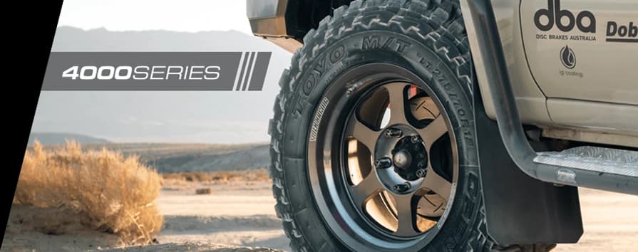 Primer plano rueda vehículo 4WD en terreno desértico con branding DBA 4000 Series prominentemente visible en carrocería, mostrando performance frenado todoterreno