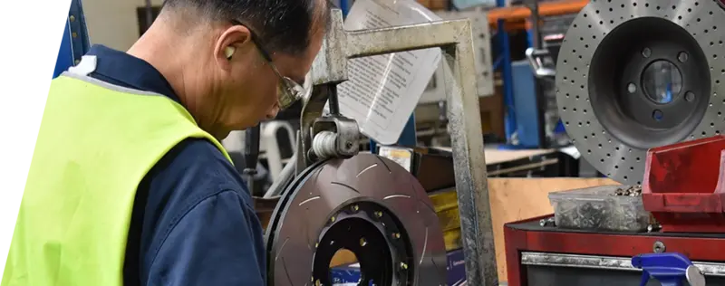 Técnico de fábrica DBA con equipo de seguridad trabajando en la producción de discos de freno con equipamiento especializado