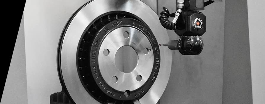 Primer plano en blanco y negro de un disco de freno DBA en instalación de fabricación con equipo especializado posicionado junto a la superficie lisa del disco