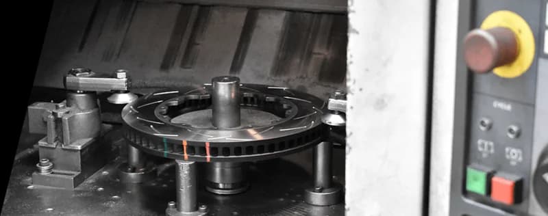 Disco de freno DBA con indicadores de temperatura de colores siendo fabricado en máquina CNC de precisión con panel de control visible