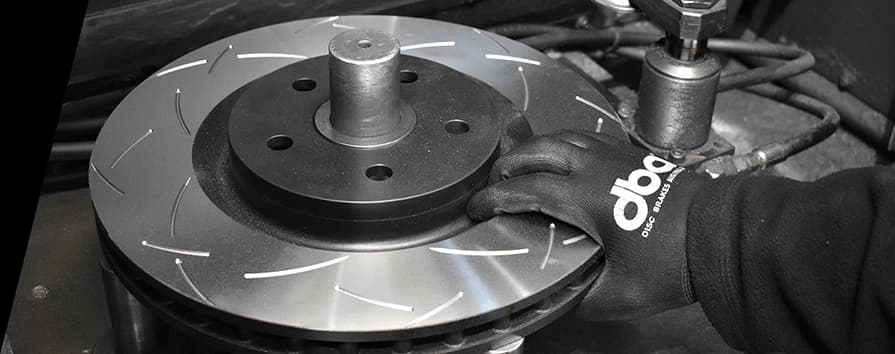 Primer plano de técnico con guantes DBA instalando un disco de freno ranurado en el buje de un vehículo durante servicio de frenos