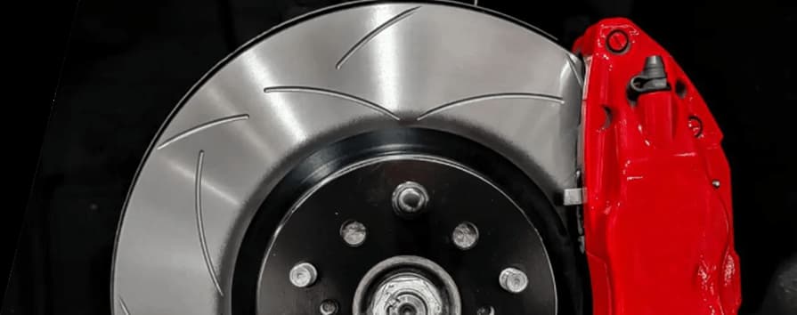 Primer plano de disco de freno ranurado DBA instalado con pinza roja brillante en buje de vehículo sobre fondo negro