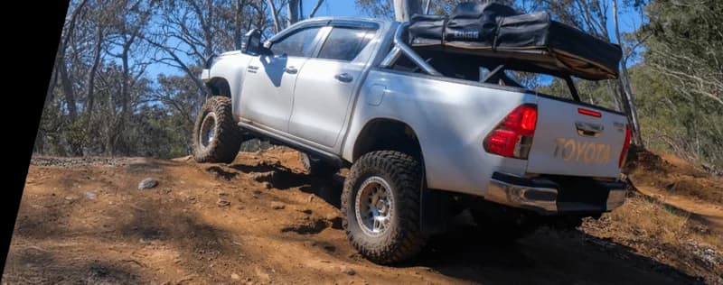 Pickup truck Toyota blanco cargado con equipo camping posicionado en terreno rocoso en monte australiano demostrando condiciones off-road carga pesada