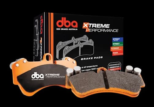 Pastillas de freno DBA Xtreme Performance con placas de respaldo naranjas y material de fricción mostradas junto a su caja de embalaje