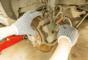 Técnica correcta para abrir válvula de purga de pinza con llave y tubo de recolección durante procedimiento de purga de frenos Manos enguantadas de mecánico abriendo válvula de purga de pinza con llave mientras tubo transparente está conectado para capturar líquido