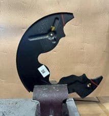 Paso 3A: Placa de respaldo retirada del vehículo y asegurada en tornillo para corte a lo largo de las líneas marcadas para espacio de pinza DBA Placa de respaldo retirada posicionada en tornillo de banco mostrando líneas de corte marcadas con rotulador listas para modificación